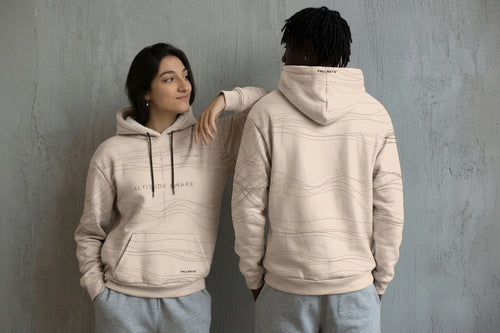 Two people wearing beige hoodies with a brand logo against a gray wall.