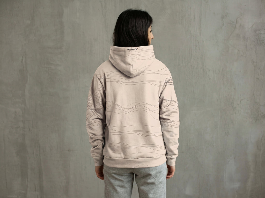 Person wearing a beige hoodie and pants against a gray wall