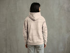 Person wearing a beige hoodie and pants against a gray wall